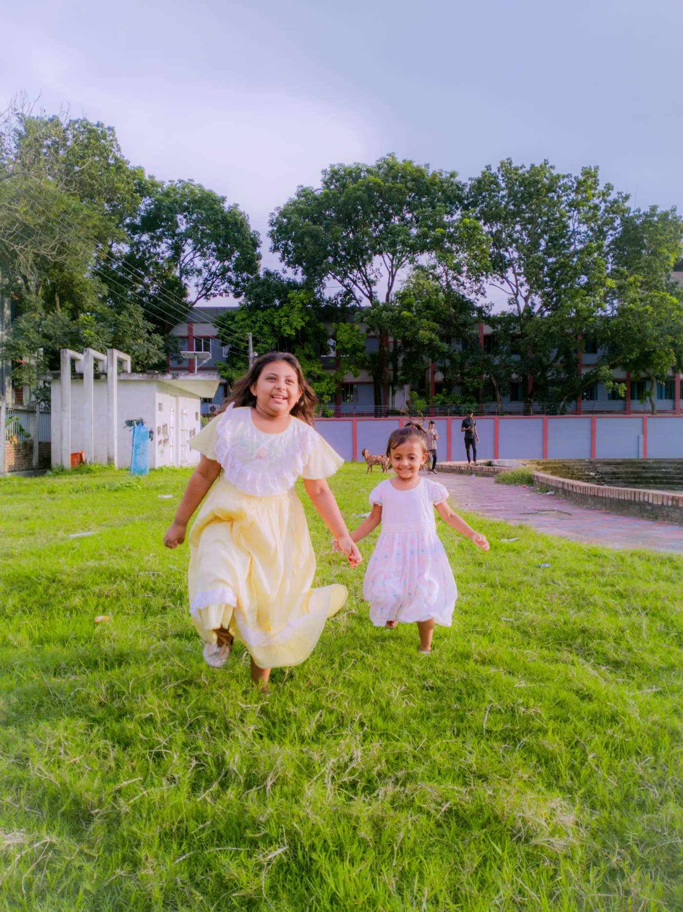 Two smiling girls holding hands as they run across a grassy field
